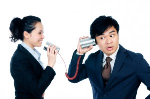 Portrait of businesswoman speaking to businessman through tin can phone on white background.